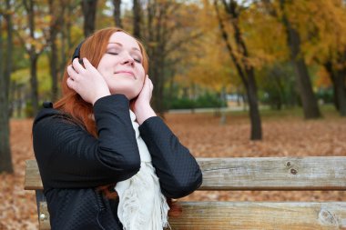 redhead girl listen music in city park, fall season clipart