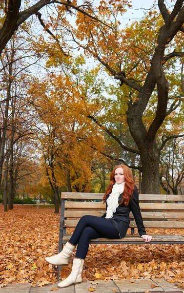 Menina ruiva sentado em um banco no parque da cidade, temporada de outono — Fotografia de Stock