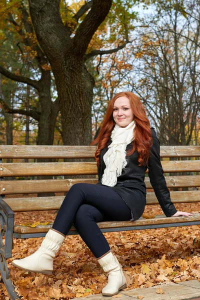 在城市公园的长椅上坐深秋季节的红发女孩 — 图库照片
