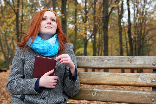 Redhead girl with book sit on a bench in city park, fall season — Stock Photo, Image