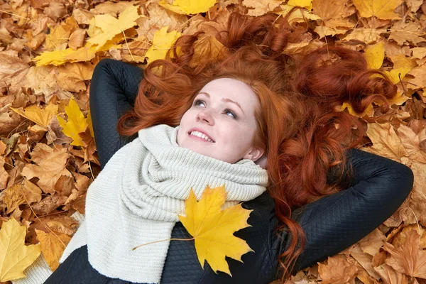 Rusovláska dívka leží na listy v městském parku, podzim — Stock fotografie
