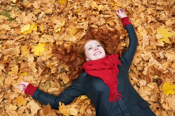 Rusovláska dívka leží na listy v městském parku, podzim — Stock fotografie