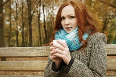 Kızıl saçlı kız şehir parkta bir bankta oturup çay fincan ile sonbahar sezon