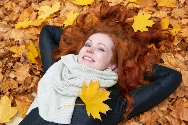 Rusovláska dívka leží na listy v městském parku, podzim — Stock fotografie