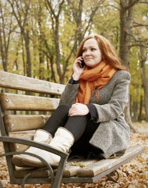 Kızıl saçlı kız kıza telefon ve şehir parkta bir bankta oturmuş sonbahar sezon