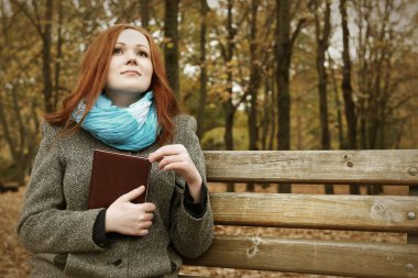 Kızıl saçlı kız şehir parkta bir bankta oturup kitap ile sonbahar sezon