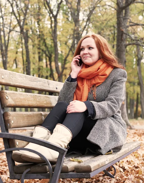 Rothaarige Mädchen telefonieren und sitzen auf einer Bank im Stadtpark, Herbstsaison — Stockfoto