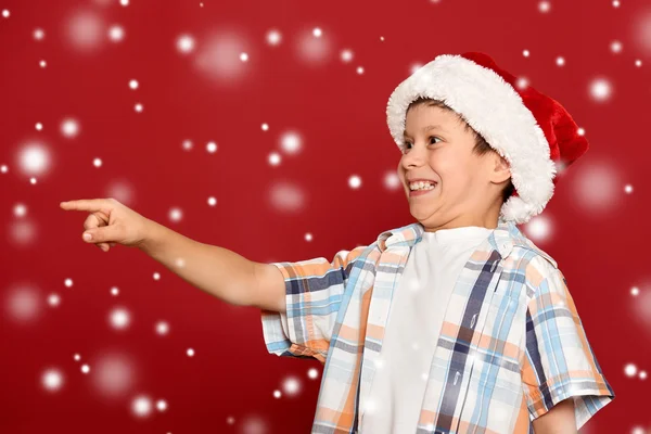 Weihnachtskonzept für den Winterurlaub - Junge mit Weihnachtsmannmütze zeigt auf sein Handy — Stockfoto