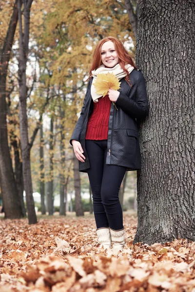 Рыжая девушка с листьями в городском парке, осенний сезон — стоковое фото