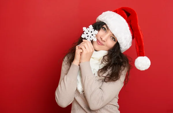 Bella giovane donna ritratto in cappello Babbo Natale helper con grande fiocco di neve in posa sul rosso — Foto Stock