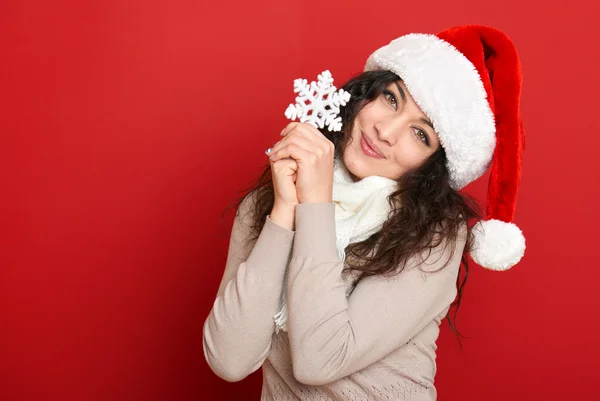 Mooie jonge vrouw portret in helper kerstmuts met grote sneeuwvlok poseren op rood — Stockfoto