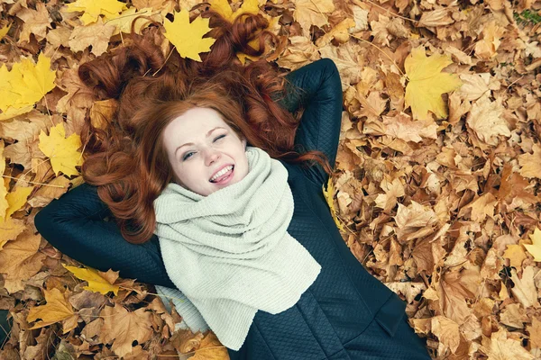 Rusovláska dívka leží na listy a mrknutí v městském parku, podzim — Stock fotografie