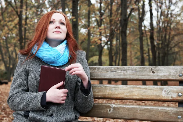 Redhead girl with book sit on a bench in city park, fall season — Stock Photo, Image