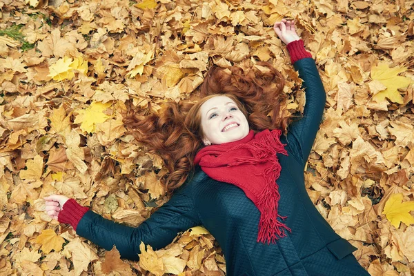 Rusovláska dívka leží na listy v městském parku, podzim — Stock fotografie