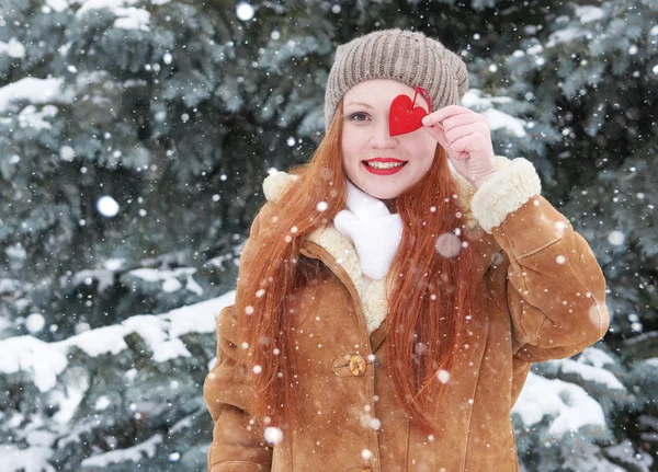 Jonge vrouw poseren met rood hart speelgoed. Winterseizoen. Outdoor Portret in park. Besneeuwde weer. Valentine concept. — Stockfoto