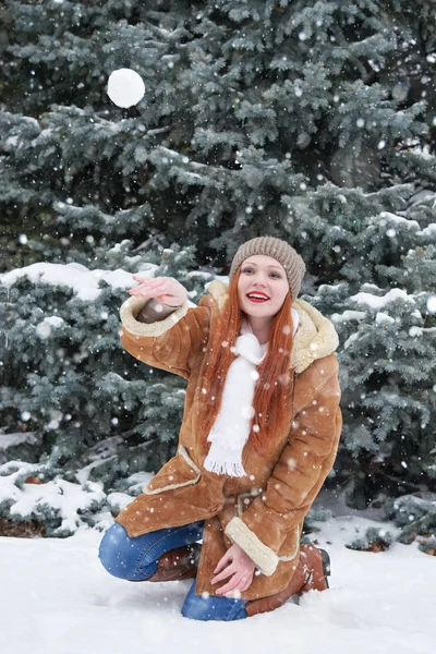 Chica jugar bolas de nieve en el bosque de invierno en el día. Abeto con nieve. Pelirroja mujer longitud completa . — Foto de Stock