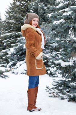 Kız kış parkta gün poz. Kar köknar ağaçlarıyla. Kızıl saçlı kadın tam uzunlukta.