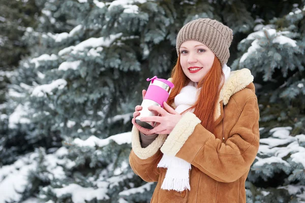 Girl get warm and drink tea in winter park. Fir trees with snow. — Stock Photo, Image