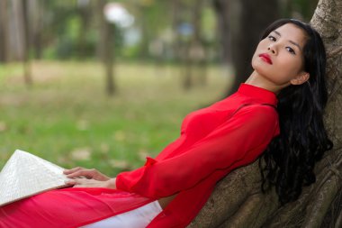 Slender young Vietnamese woman relaxing in a park clipart