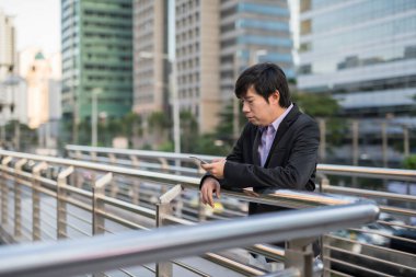 Modern şehirde uygulama ve telefon kullanarak resmi takım elbiseli Çinli bir işadamı. Ciddi girişimci, 30-40 yaşları arasında orta yaşlı, akıllı telefondan iş projesini kontrol ediyor..