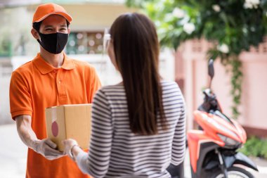 Maskeli ve üniformalı gülümseyen teslimatçı, yüz kalkanıyla motosikletle bayan müşteriye bir paket teslim ediyor. Kal