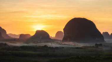 Tayland 'ın Krabi ilindeki Din Daeng (Dang) Doi' den gelen sis ve siluet karst dağlarından gündoğumu ışınları. Tayland 'ın güneyindeki ünlü seyahat beldesi..