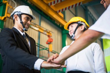 Birlik ve başarı kavramına sahip fabrika endüstriyel takım çalışması. İş adamı, kadın mühendis ve kasklı eski işçi el ele tutuşuyor..