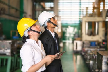 Fabrika denetçisi ve müfettiş, kalite kontrolü için fabrikanın donanım güvenliğini kontrol ediyorlar. Genç işçi sınav raporunu göndermek için kurumsal başvuru kullanmak üzere tableti elinde tut.