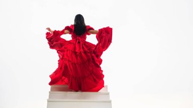 Kırmızı uzun elbiseli, beyaz arka planlı, cennete giden merdivenlerde yürüyen bir kadın. Uzayı metin için kopyala. Tatil gezisi konsepti.