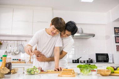 LGBT Asyalı adam sevgililer gününü kutlamak için mutfakta salata yaparken erkek arkadaşına sarılıyor. Tatlı eşcinsel çift sağlıklı beslenme tarzı. Sevgi ve mutluluk birlikte. Aynı cinsiyetten aile.