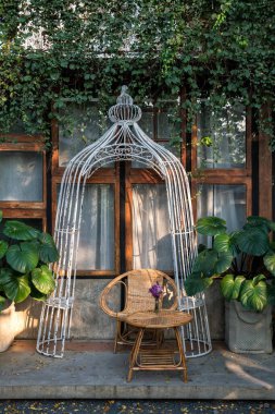 Rattan koltuğu ve pencere kenarındaki masa. Güzel bahçe dekorasyonu. Evin dışı ve tasarımı yeşil ortamda.