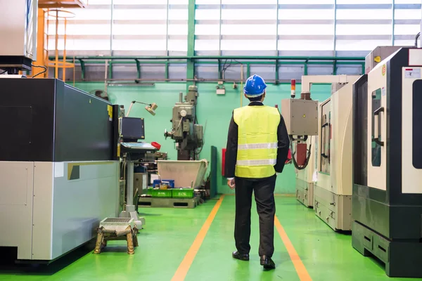 Rear of waist up inspector manager with hardhat walk along production department to check Metalworking CNC (Computer numerical control) lathe milling machine in factory. Industry auditor.