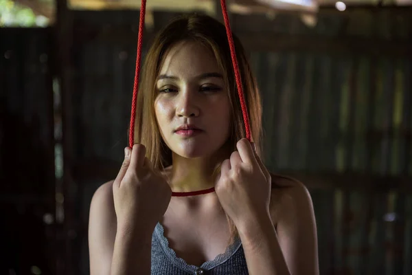 绝望的亚洲年轻女人把红绳绑在脖子上 挂在废弃的房子里自杀 爱情心碎 沮丧或失业以及痛苦的概念 免版税图库照片