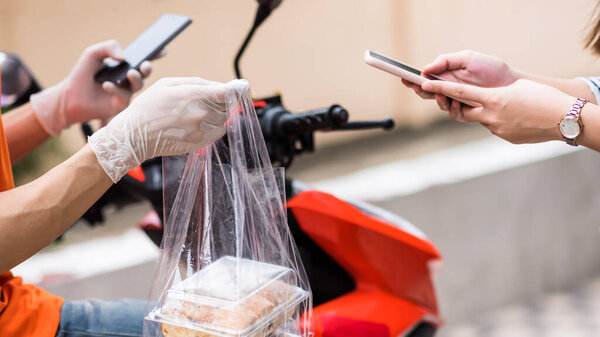 Customer press payment and confirm to receive food on smartphone app while courier deliveryman with gloves on motorbike giving bag of sweet bakery. New normal famous business of online order.