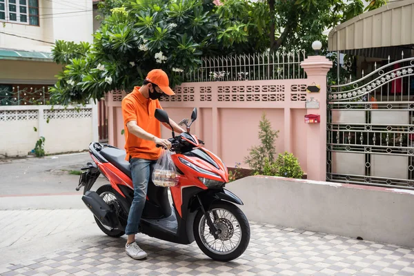 食品配達スタッフはオンラインで顧客の注文食品にパン屋を提供するためにバイクに乗る 彼はアパートの前にオートバイを停め 客が迎えに来るのを待つ Covid 19パンデミック時の新しい通常業務は ストック写真