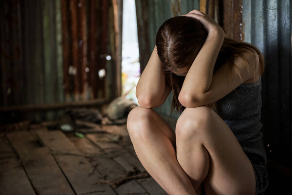 Young Asian woman hands touch her head and sit in abandoned house. Mental Post Traumatic Stress PTSD disorder or sickness, jobless, drug addiction, or heartbreak from love concept.