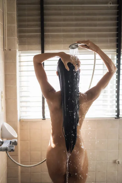 亚洲性感的棕褐色女人在靠近窗户的浴室里用自然光冲洗黑色长发 裸女淋浴在运动喷雾水 保健和卫生生活方式 — 图库照片