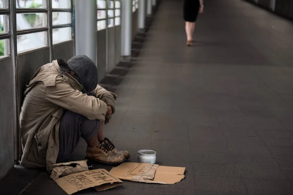无家可归的老人或乞丐低着头 拿着捐赠的碗坐下来 帮助签横幅 贫穷者在冬天睡觉 感到寒冷 退休老年人的社会问题概念 但没有钱 图库照片