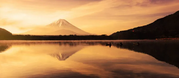 山梨県の日の出の夜明けに ボートに乗っている3人の漁師と庄司湖の霧を持つ富士山 水の上に美しいスカイラインの反射と風景 富士五湖の一つ ストックフォト