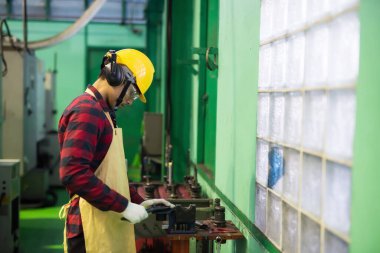 Skill mechanic worker working manual on lathe spare part metal in iron manufacturing factory. Man with hardhat, gloves, and uniform plaid red shirt.