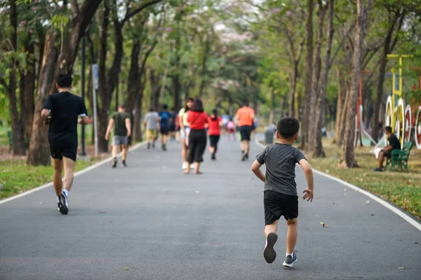 Little fit Asian boy run fast on park running track with many adult runner. Bodybuilding, kid sport, and healthy lifestyle concept. Back view.