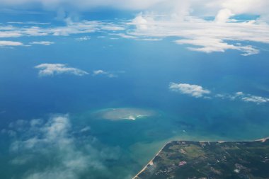 Tayland 'da yaz güneşli bir günde Phuket Sahili ve andaman Okyanusu' nun uçak penceresinden deniz manzarası. Kabarık bulutlar arasında deniz kıyısında uçuyor