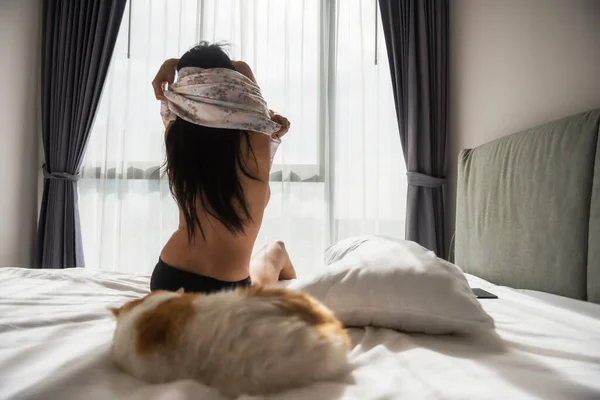 背の高いセクシーなアジアの女性は 太陽の光に対して早朝にベッドの上で寝て黄色のエキゾチックな短い髪の猫とパジャマを脱ぎます 寝室の魅力的なタンの女の子 舞台裏で — ストック写真
