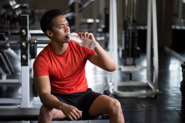 Young Asian strong muscular handsome man drink water in fitness gym after break from work out exercise. Bodybuilding and healthy lifestyle concept.