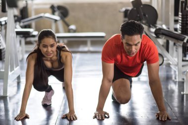Young Asian couple stretching legs and feet to warm up before exercise in gym. Sport bodybuilding and healthy lifestyle concept.