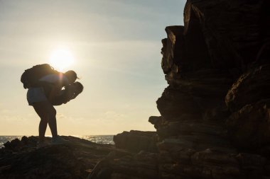 Silhouette mom kiss and hug her child boy at beach shore arch with sunset sea, Khao Laem Ya national park, Rayong, Thailand. Summer family holiday vacation in Siam, tropical country.