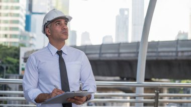 Kıdemli 50 'lerin Amerikan mühendis müdürü modern şehirdeki kağıt planlar hakkında notlar alıyor. Mühendislik araştırması ya da şehirdeki inşaat alanındaki gelişmeleri kontrol etmek.