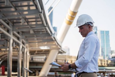 50 'lerin son sınıf Amerikalı mimar mühendis yöneticisi modern şehirdeki kağıt planlar üzerine notlar yazıyor. Mühendislik sitesi tetkiki ya da taslak işlemleri kasabada devam ediyor.