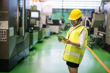 Asyalı gülümseyen işçiyi kasketli ve koruma gözlüklü olarak fabrika atölyesinde fotokopi alanı olan transistör mikroçip makinelerini kontrol etmek için tablet kullanarak beline yerleştir. Teknoloji ile sanayi üretimi.