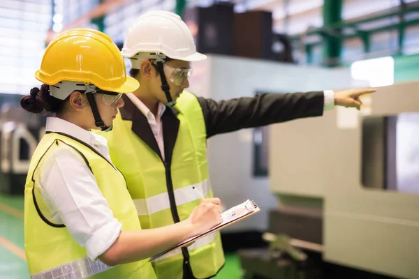 Kadın fabrika müfettişi denetim sonuçlarını yazarken yönetici otomatik fabrika makinelerini işaret ediyor. CNC otomatik torna makineleriyle sanayi üretimi. Kalite güvencesi (QA).